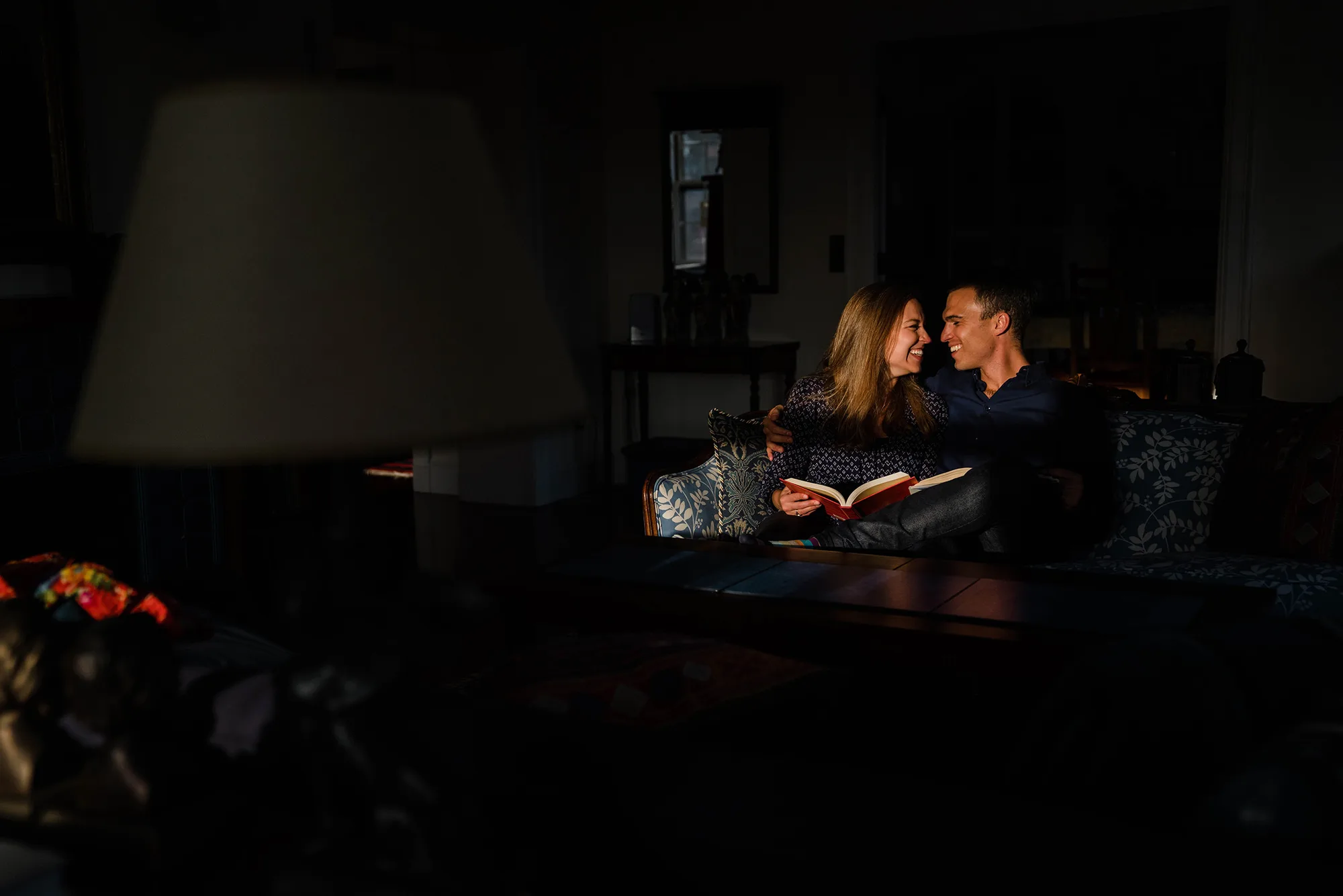 A best of Boston Engagement photograph of a couple laughing together at home while they relax on the couch together.