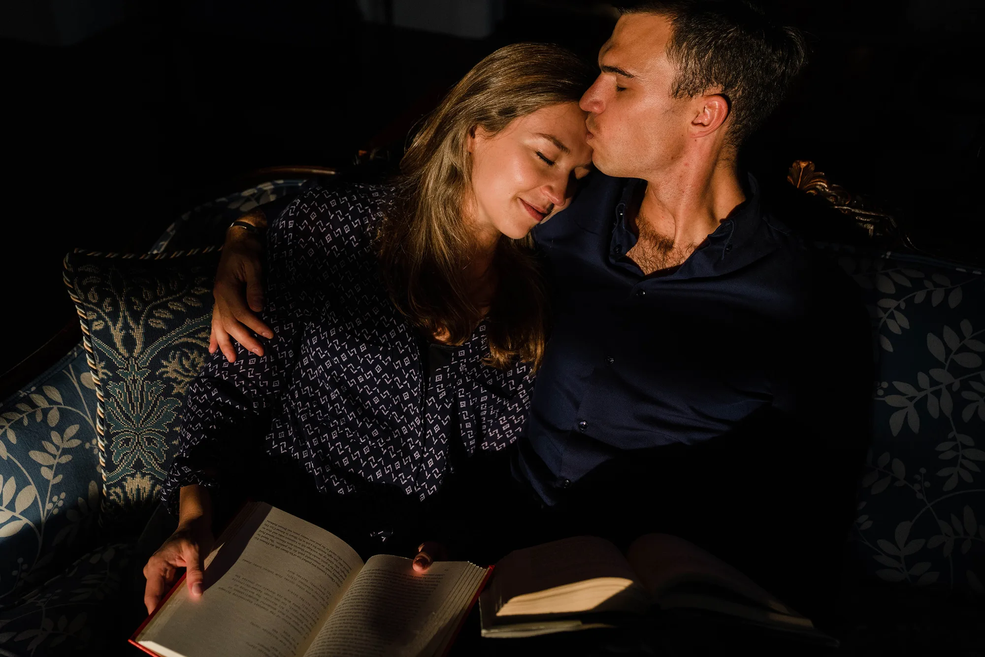A documentary photograph of a couple cuddling as they sit on the couch and read together during an in home engagement session in Boston
