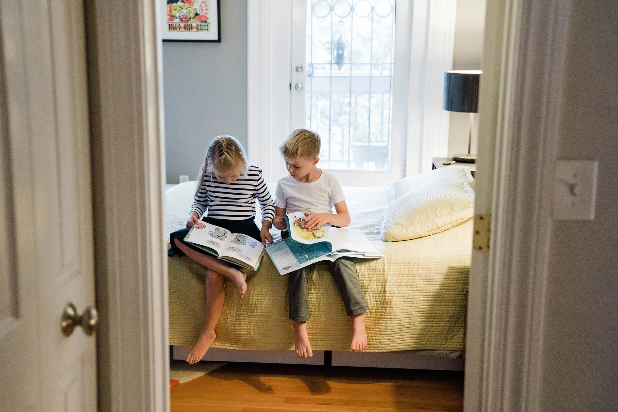 A best of Boston photograph of a brother and sister reading books in their parents bedroom during an in home family session in Boston