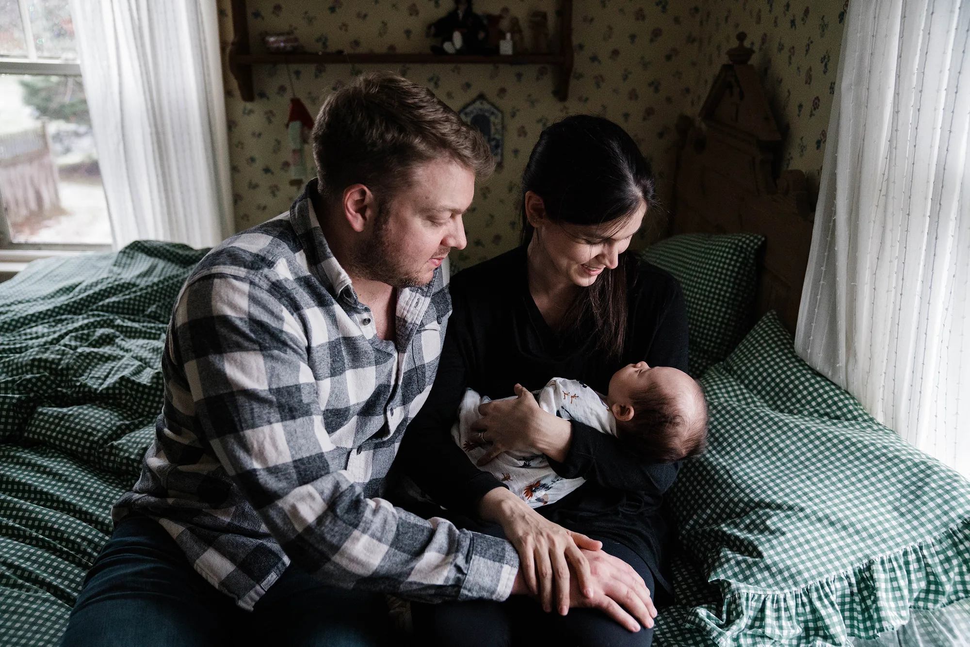 A documentary photograph of new parents watching their baby sleep during an in home family session in Boston