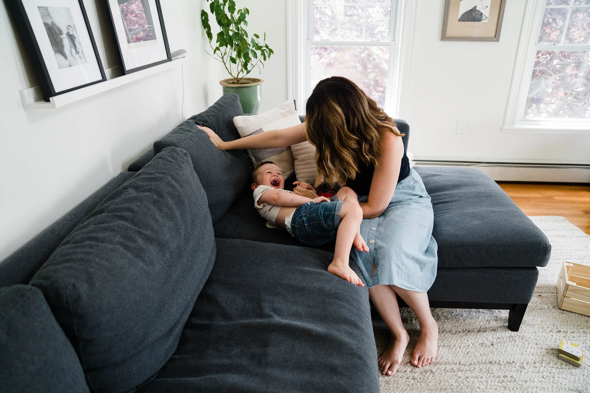 A documentary photograph of a mom playing with her son on the couch during an in home family session in Boston.