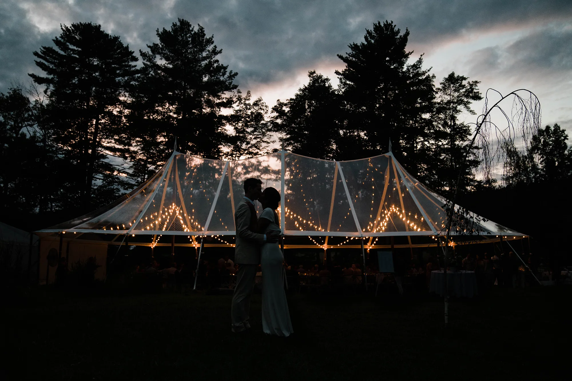 A documentary photograph featured in the best of wedding photography of 2019 showing a couple kissing outside the tent during their wedding reception
