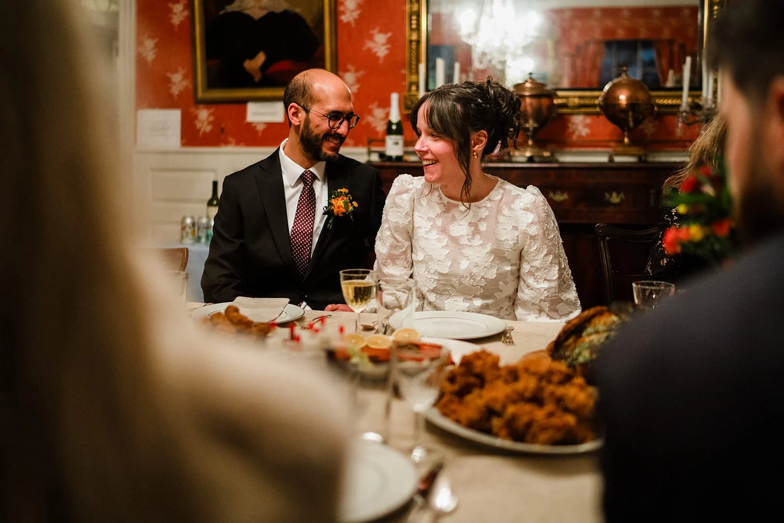 A documentary photograph of a bride and groom talking and laughing with guests during the dinner portion of their Loring Greenough House Wedding.