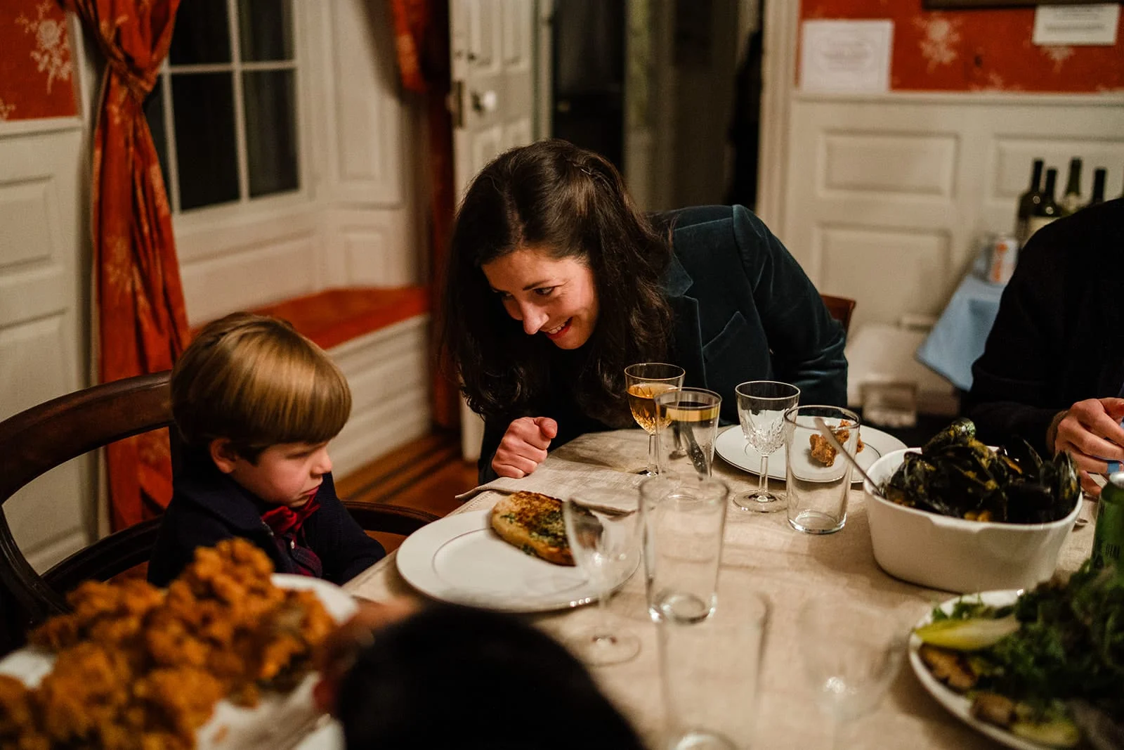 A documentary photograph guests talking and laughing during the dinner portion of a Loring Greenough House Wedding.