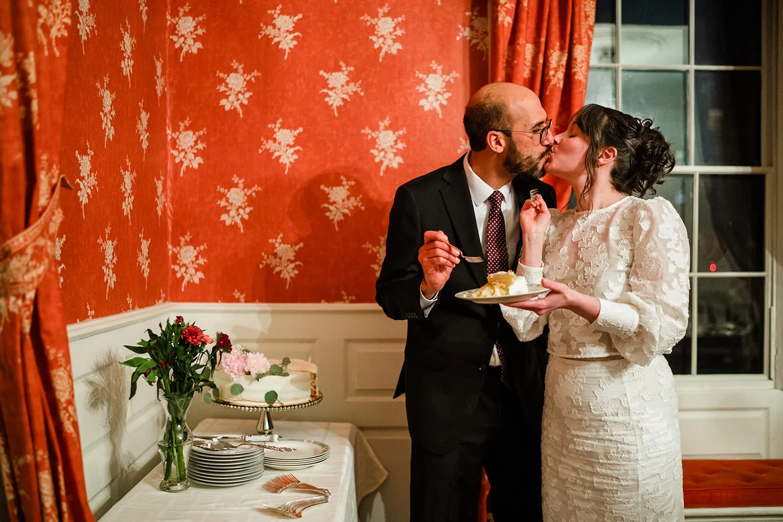 A documentary photograph of a bride and groom kissing after cutting the cake during their Loring Greenough House Wedding.