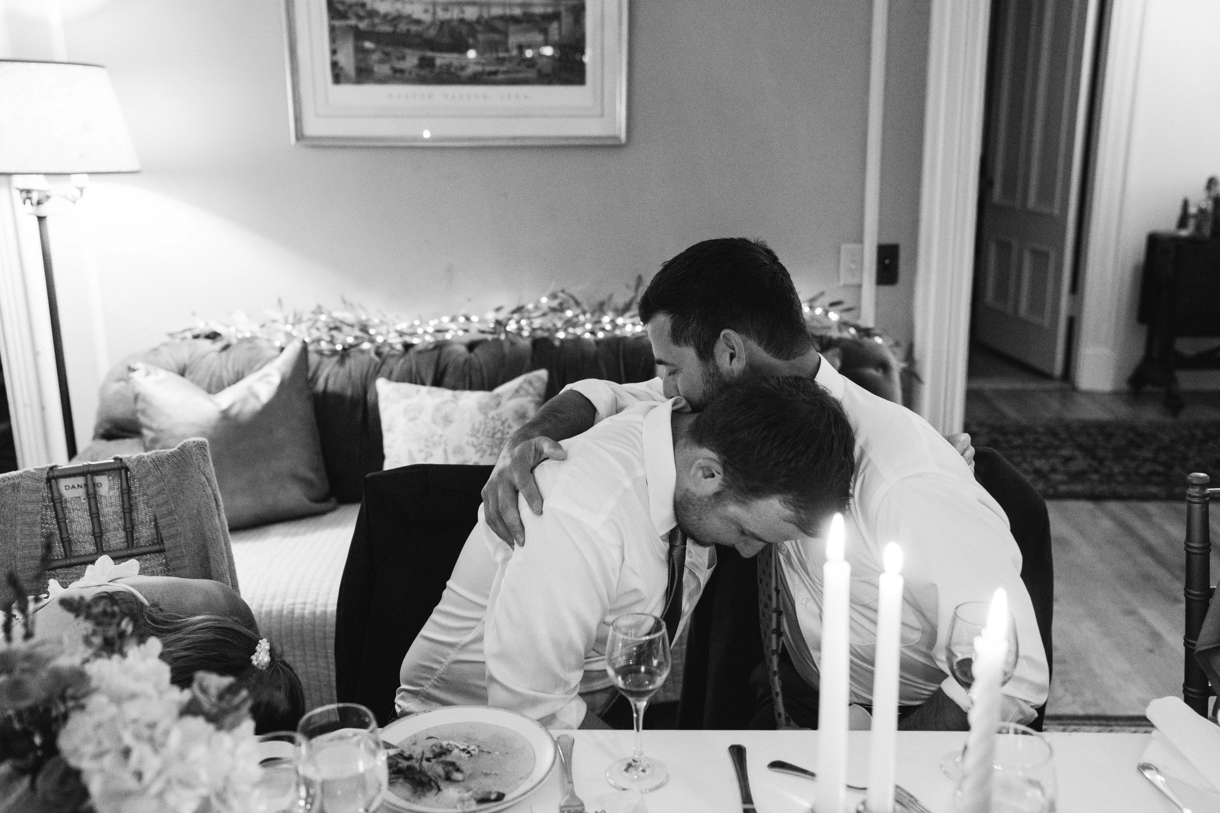 A man leaning in to hug someone across a candlelit table