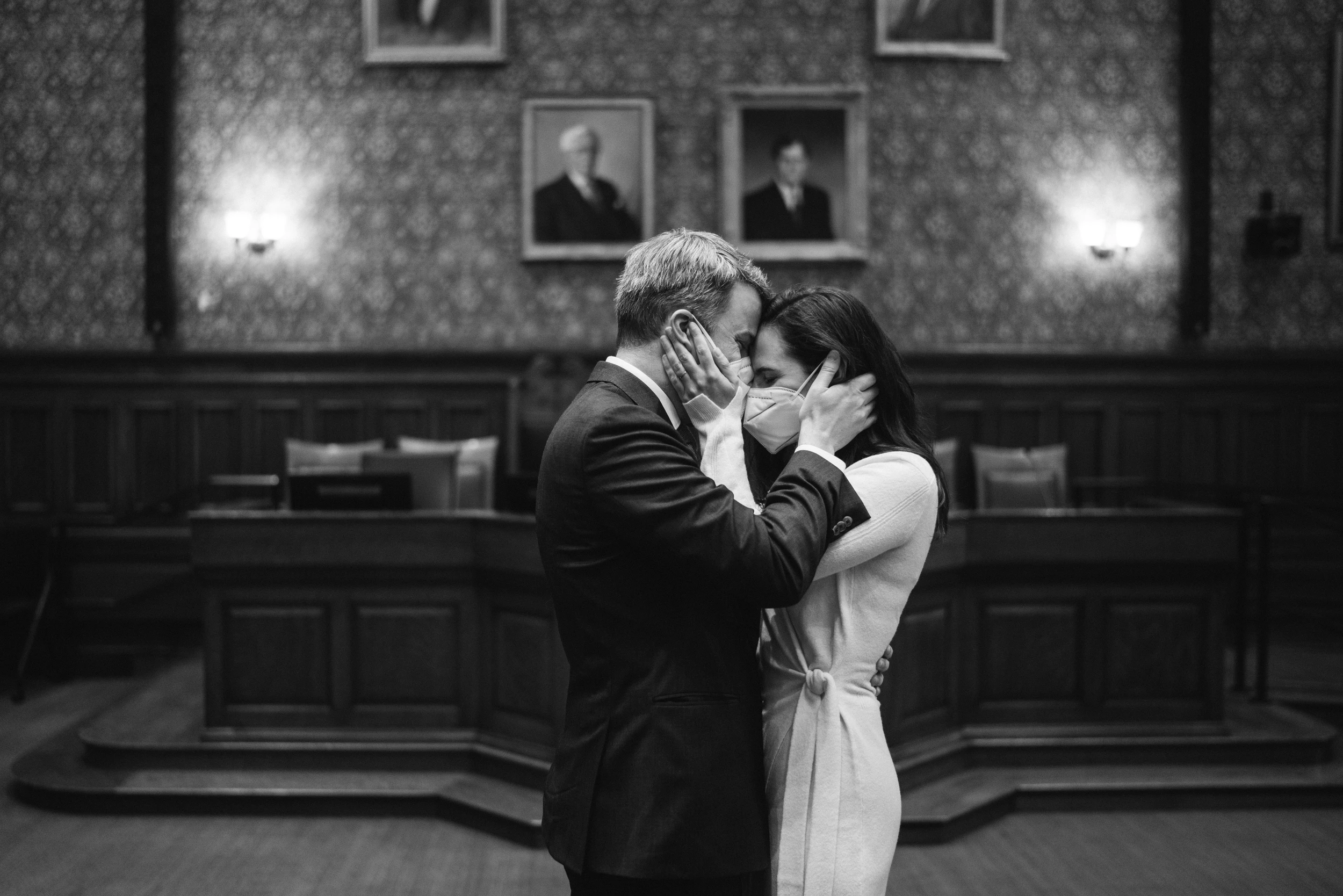 The couple kissing in a wood-panelled room under framed portraits