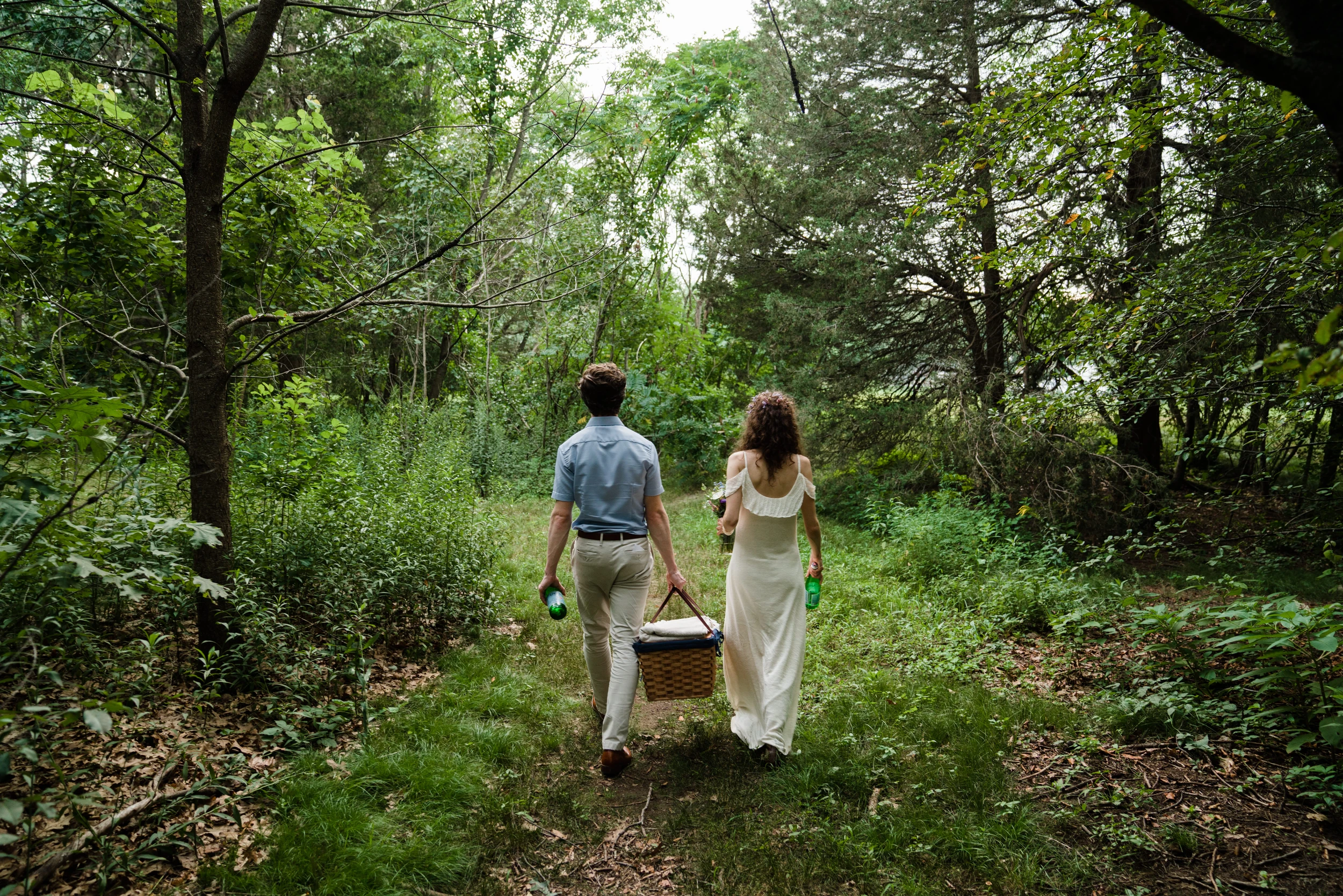 The couple walking a path through green woods, carrying a basket between them