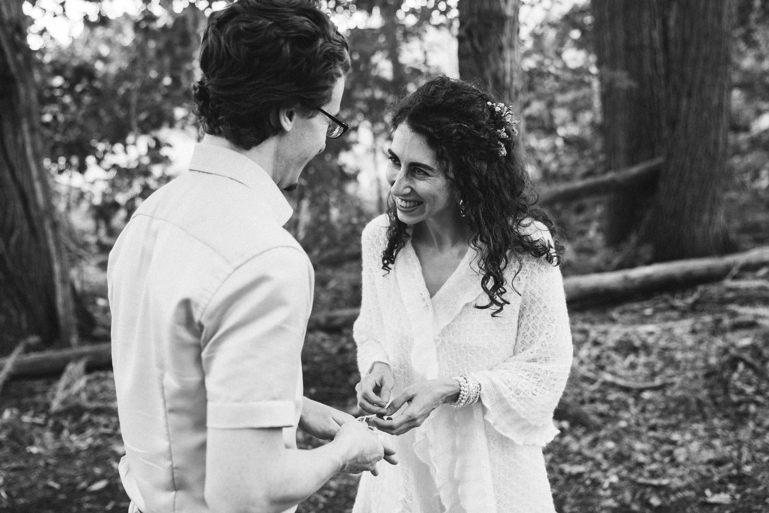 Bride in a lace dress smiling at the groom as they hold hands among trees