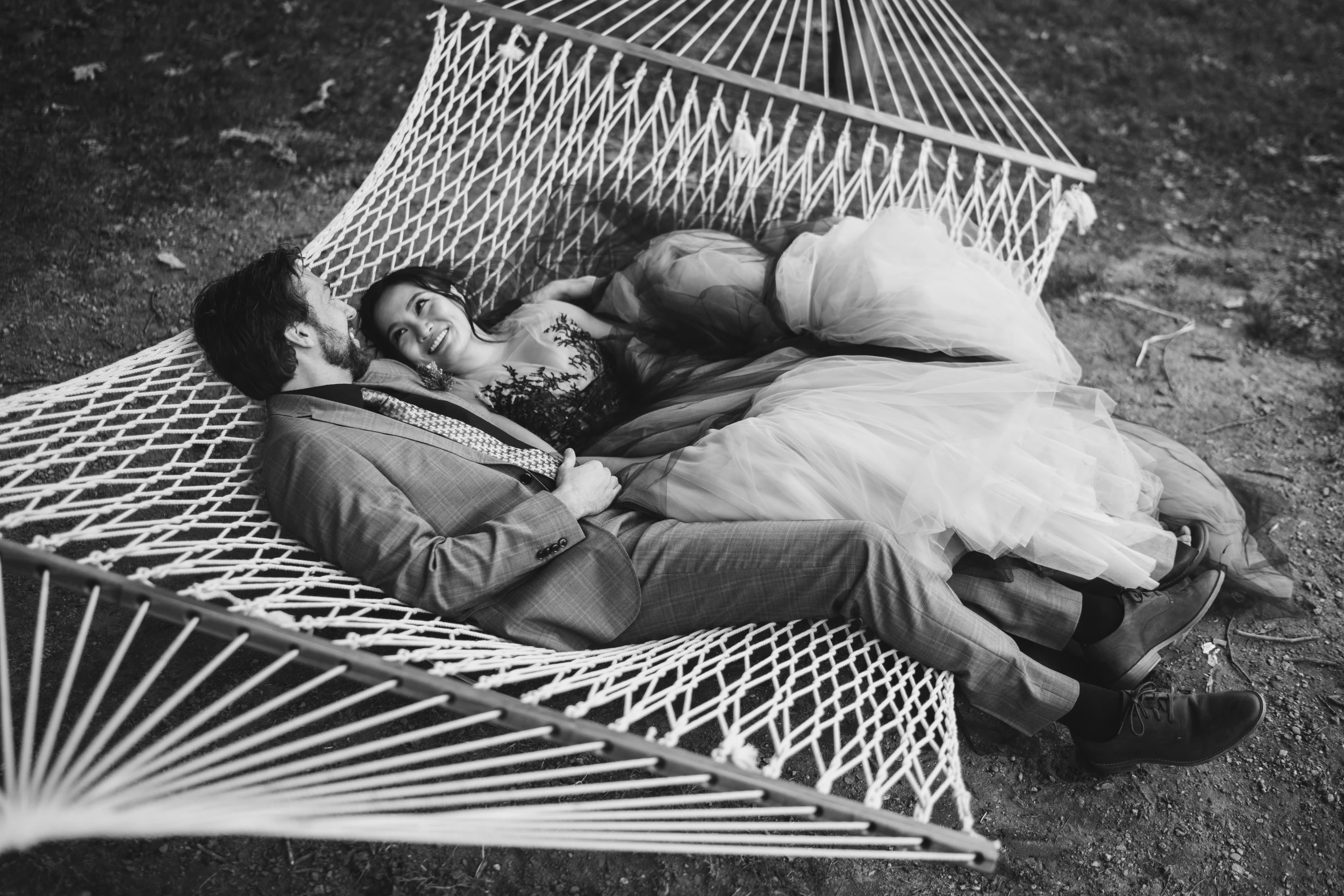 Couple lying in a rope hammock seen from above, bride in a tulle gown smiling up at the groom