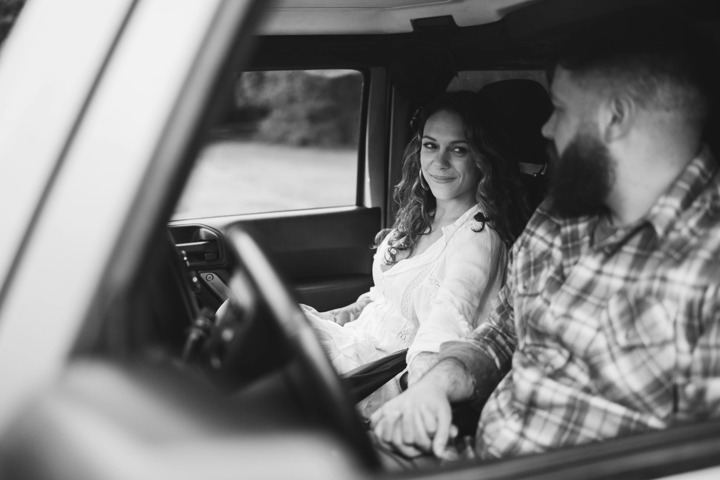Couple holding hands in the front seats of a vehicle, seen through the driver's window, she glances at him