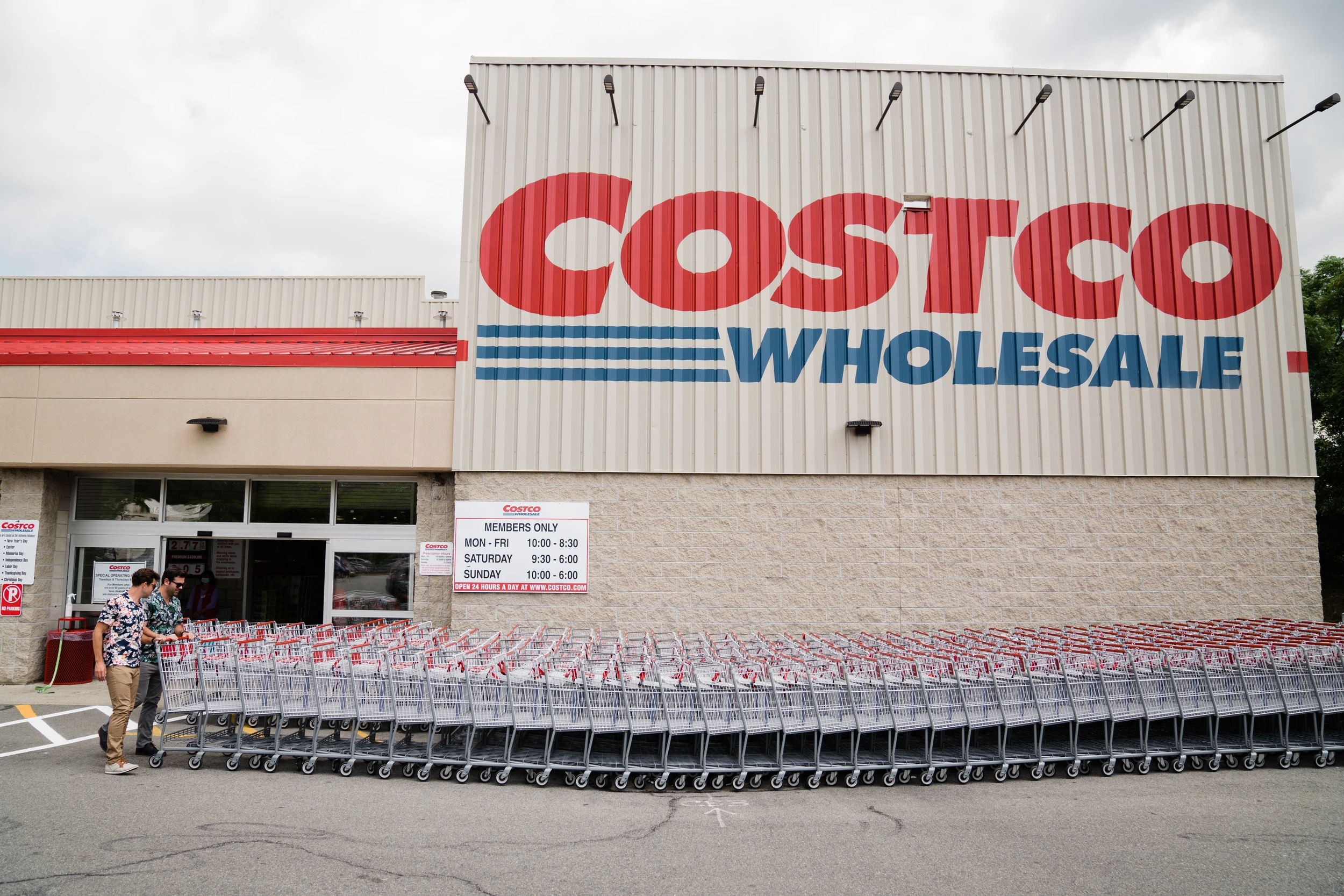 Two men in floral shirts pushing a long line of shopping carts below a giant COSTCO WHOLESALE sign