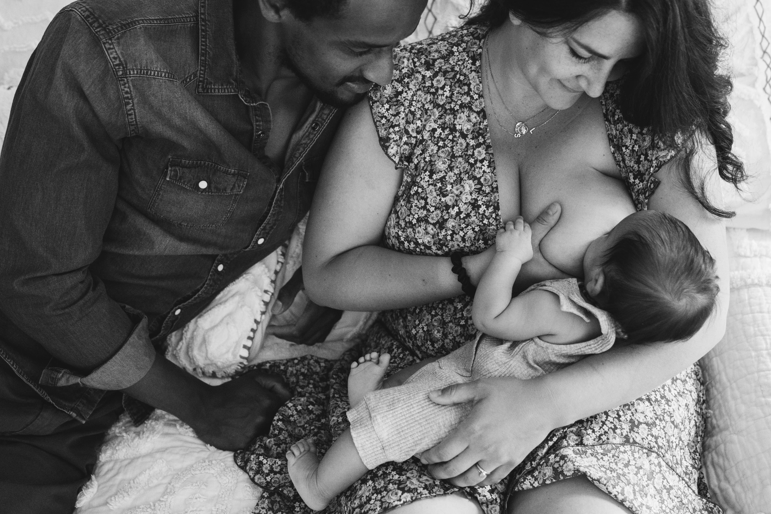 Mother breastfeeding a baby while the father leans in close, seen from above