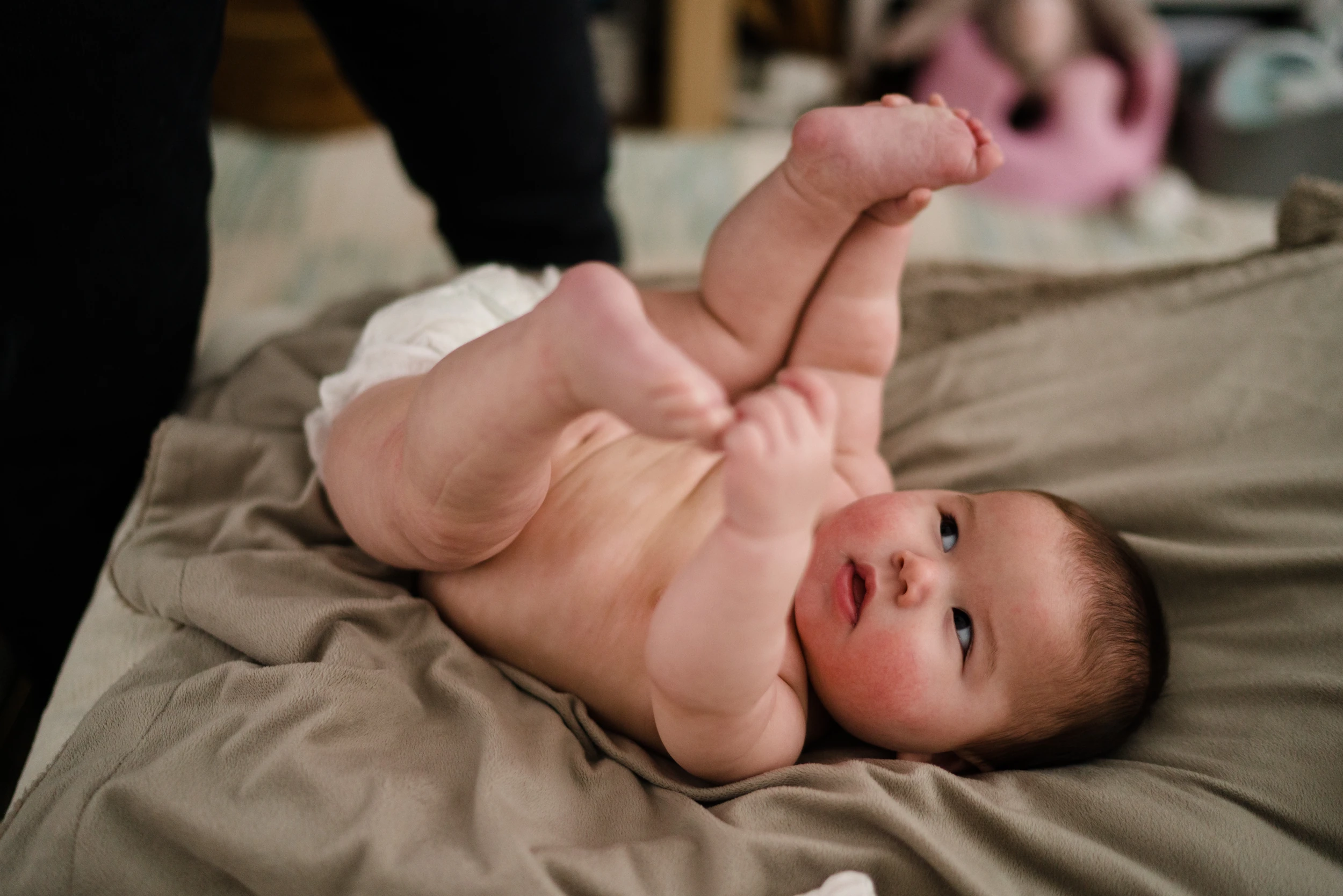 Baby lying on a blanket holding its feet in the air, looking up