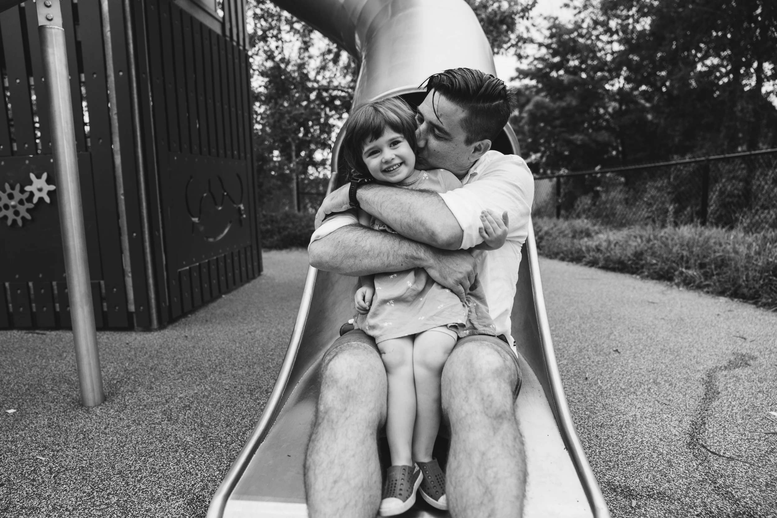 Father kisses a laughing daughter as they sit together at the bottom of a slide