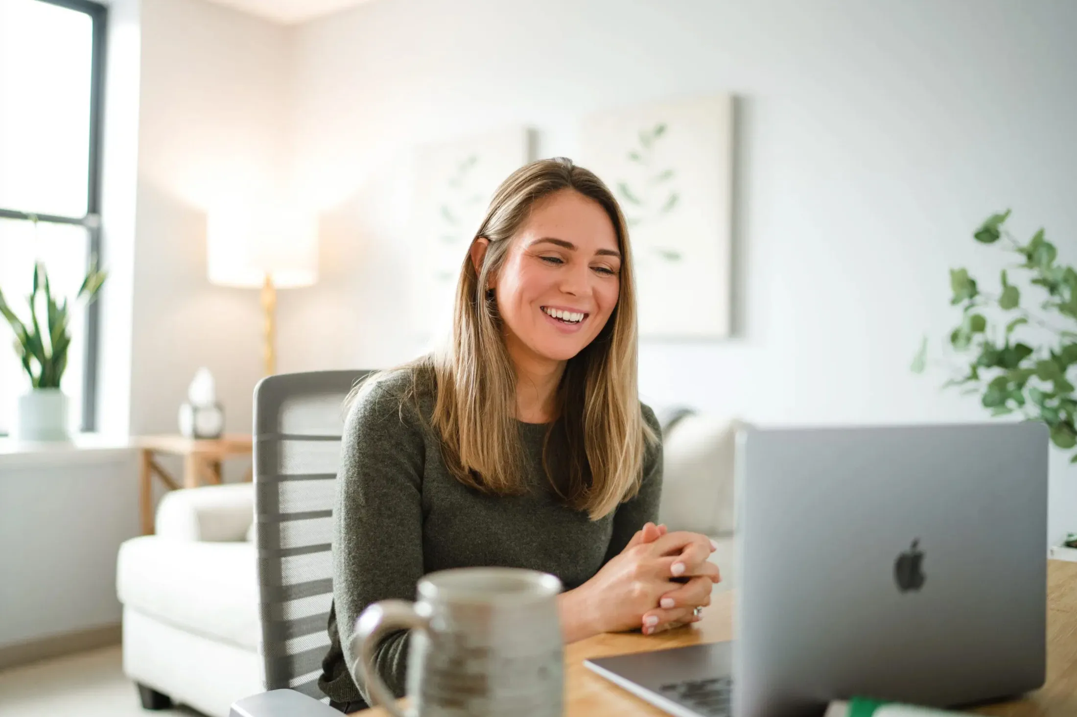 Woman laughing at a laptop on a desk in a bright room