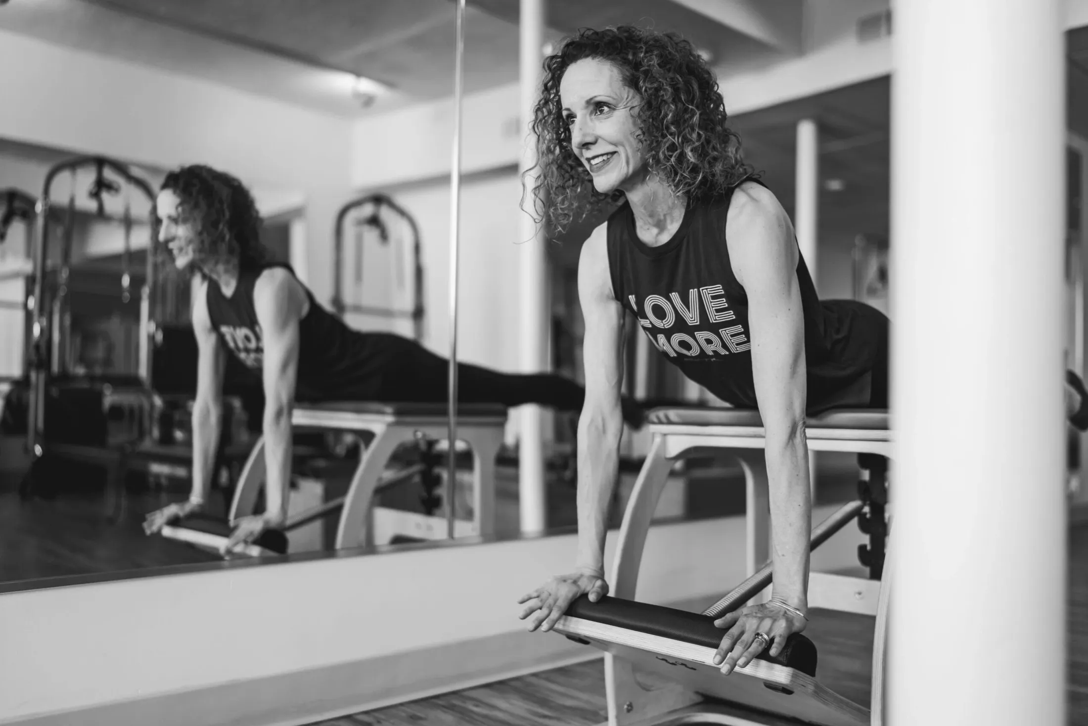 Woman on a Pilates reformer, her reflection in the mirror beside her
