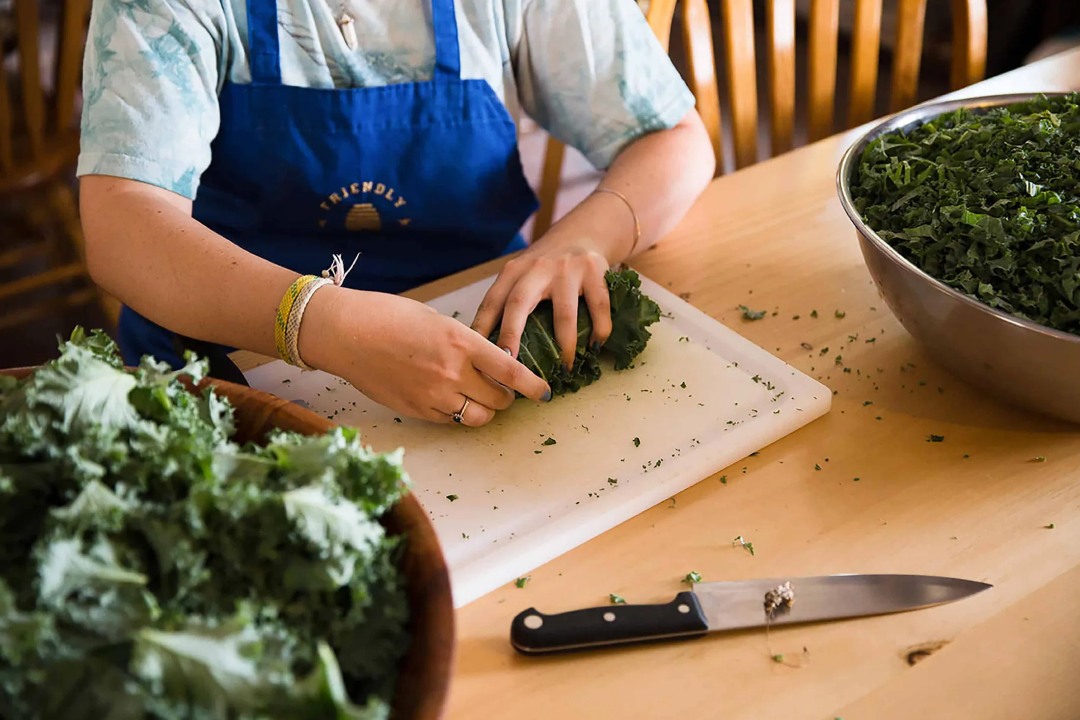 Person in a blue apron chopping kale at a wooden counter