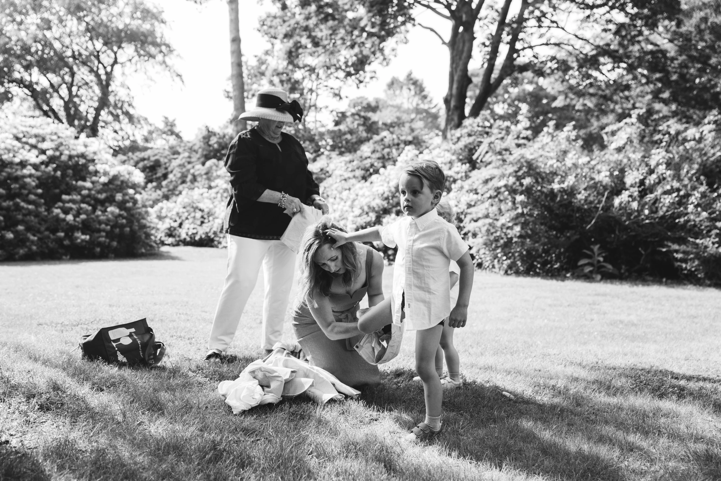 Guests helping on a sunlit lawn, one kneeling at the hem of a dress