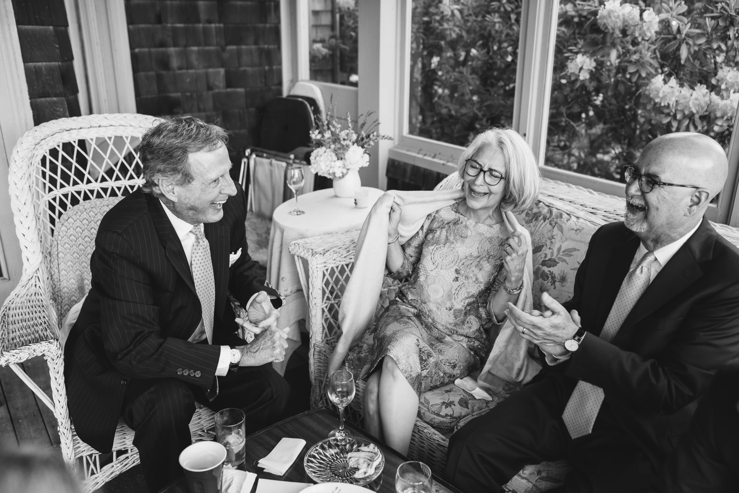 Two older men and a woman laughing together on a wicker sofa