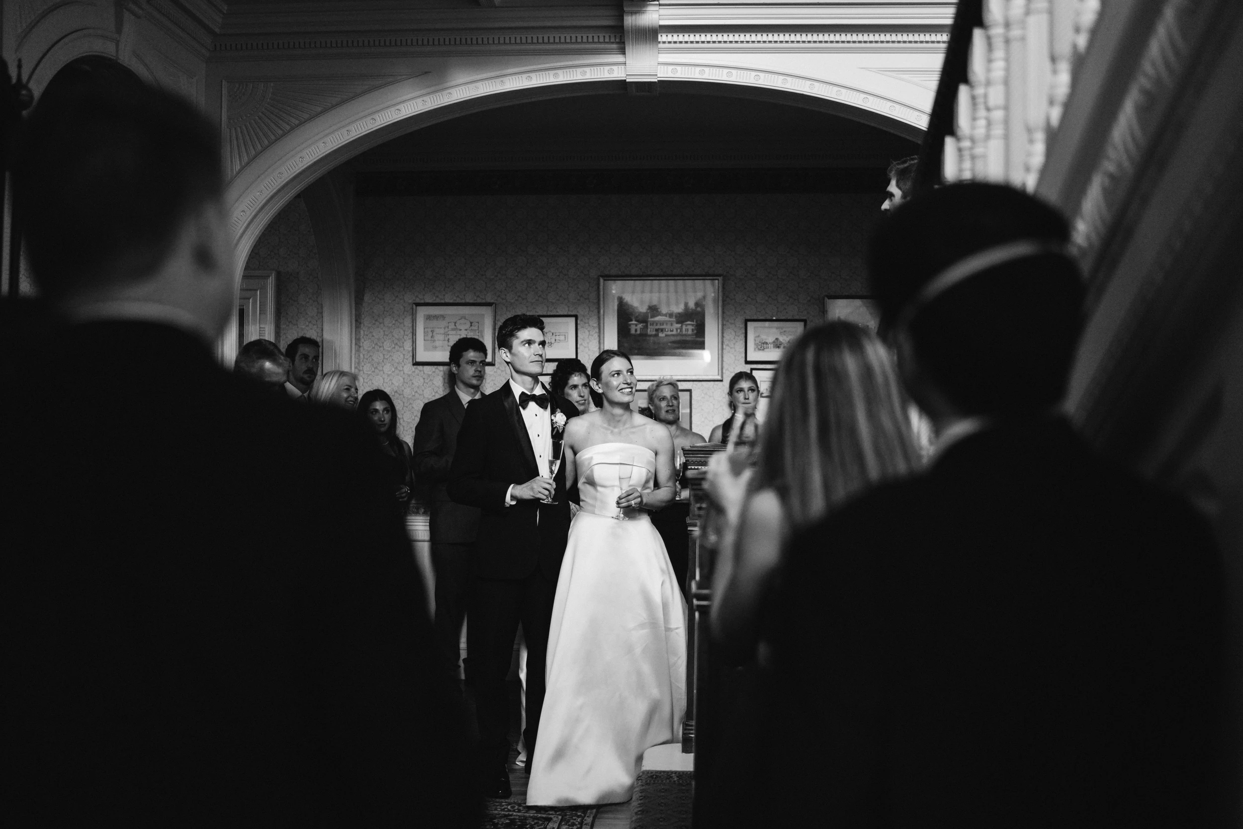 Couple under an archway looking up, guests silhouetted in the dark foreground