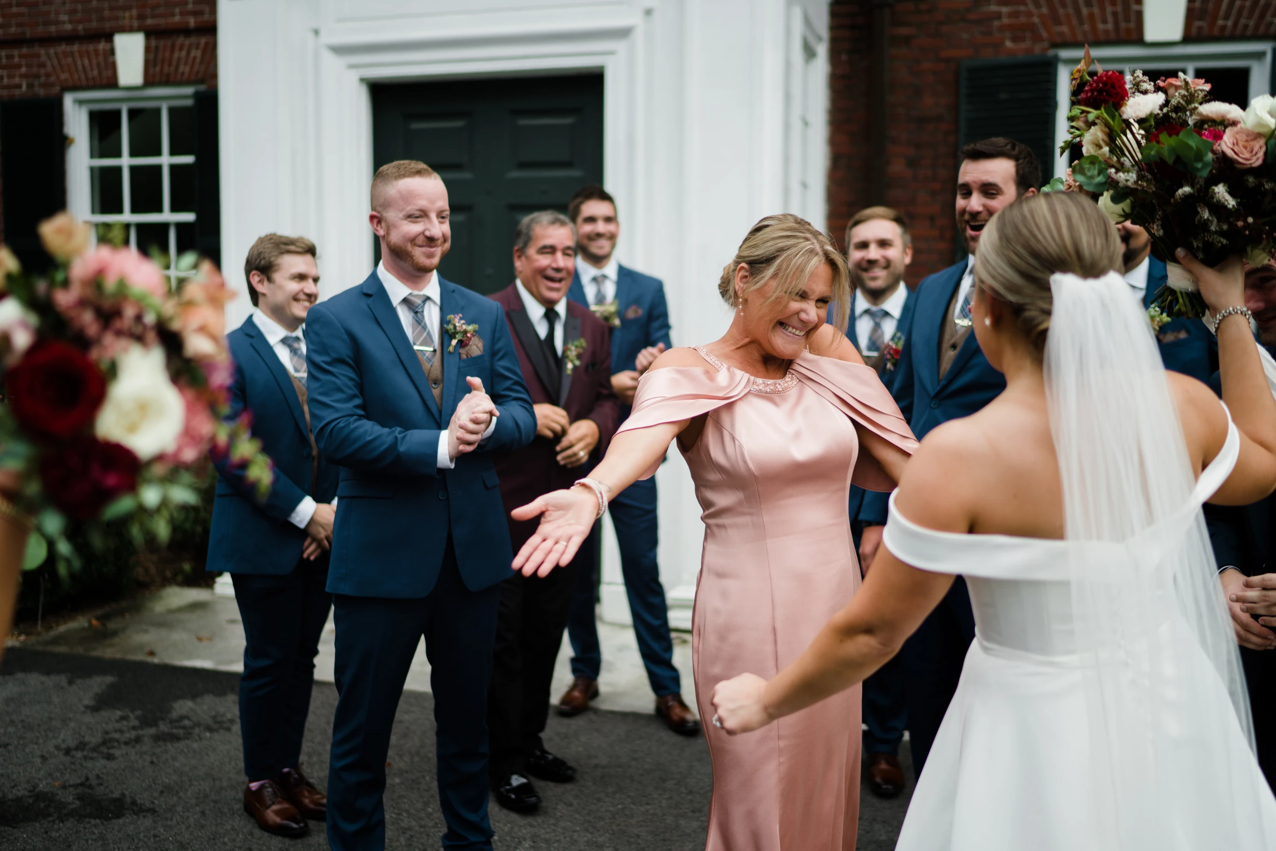 The couple stepping out to cheering friends, a bridesmaid in pink with her arms open