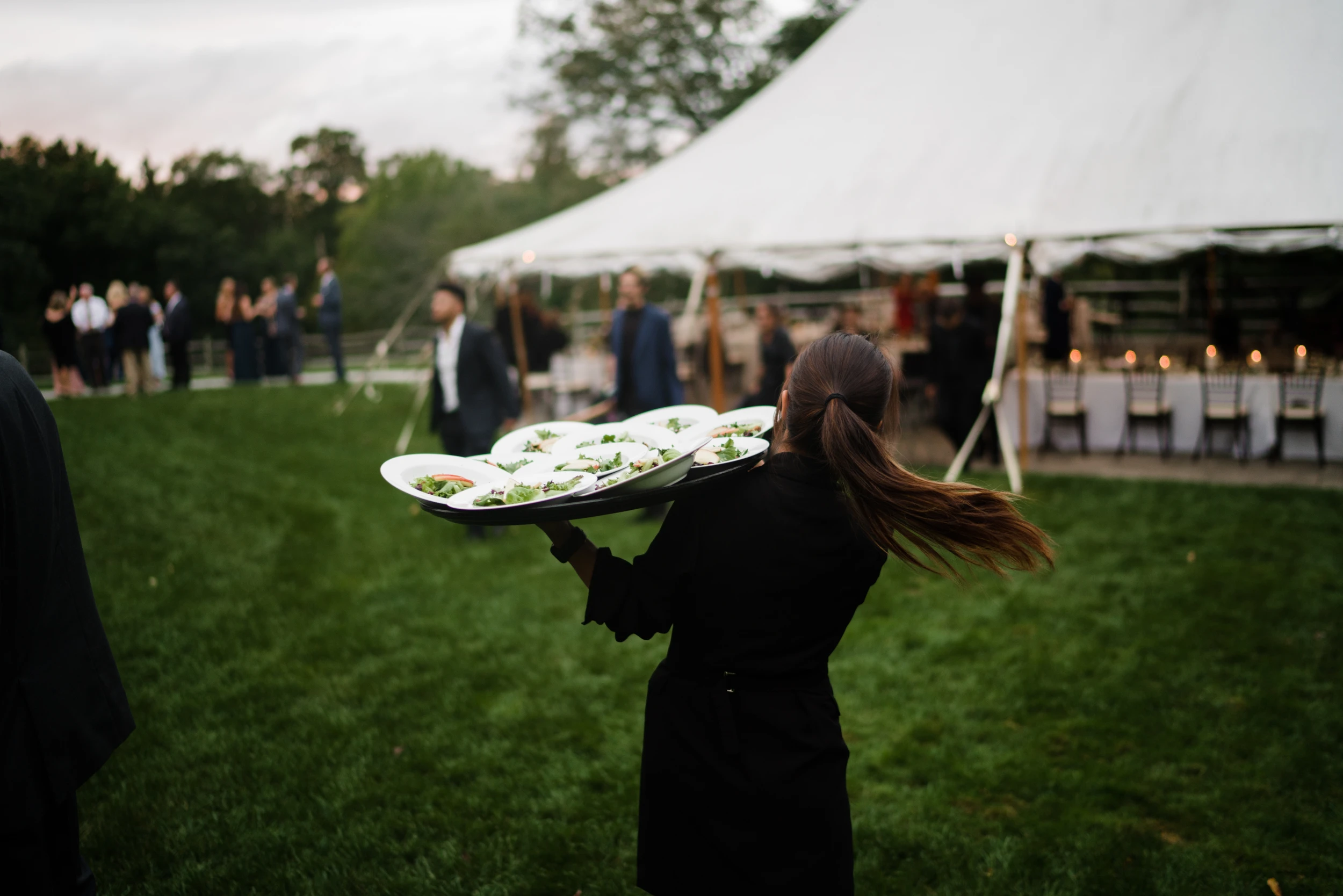 A server crossing the lawn with a tray, the reception tent behind