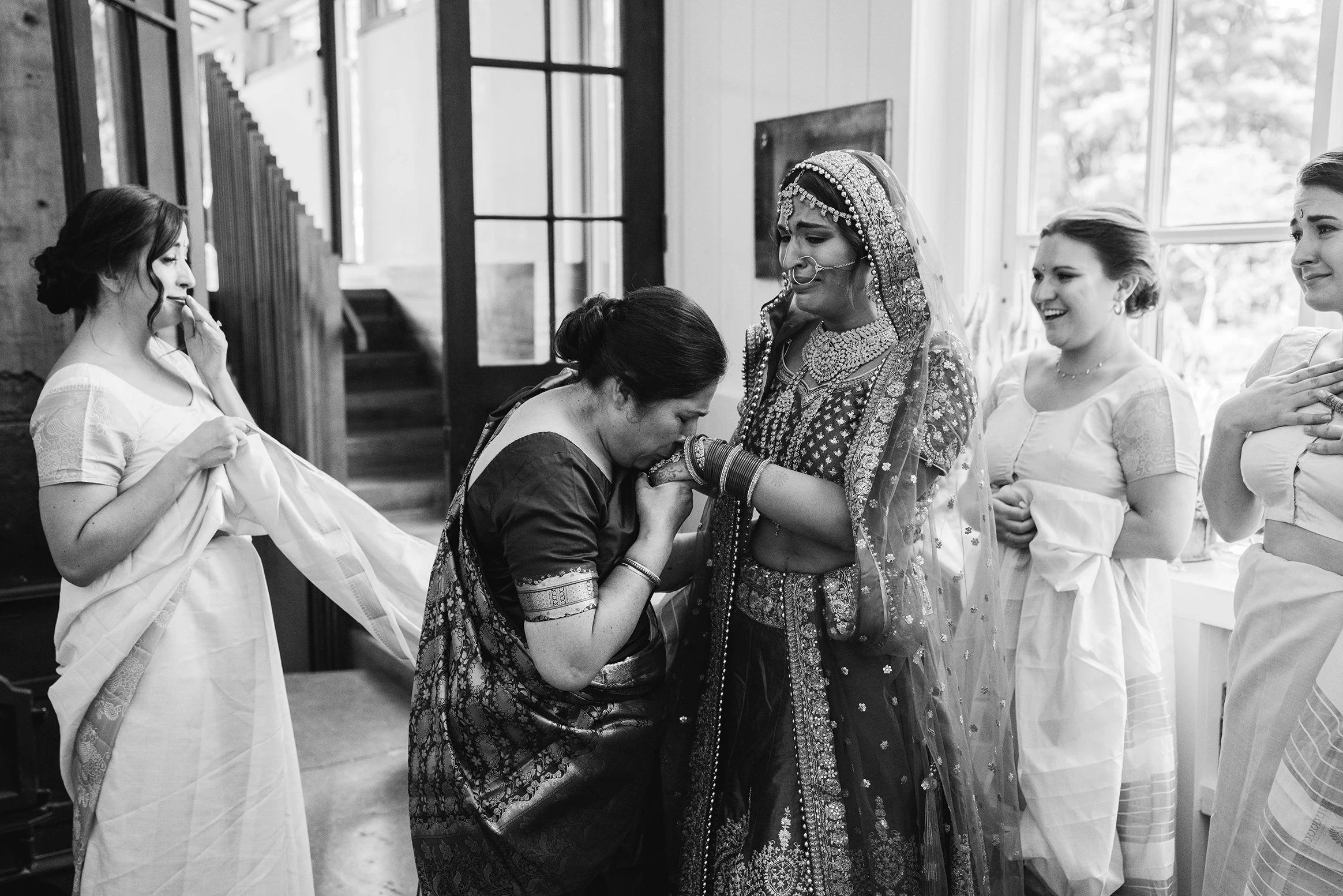 A bride in red and gold laughing as women of her family gather round her