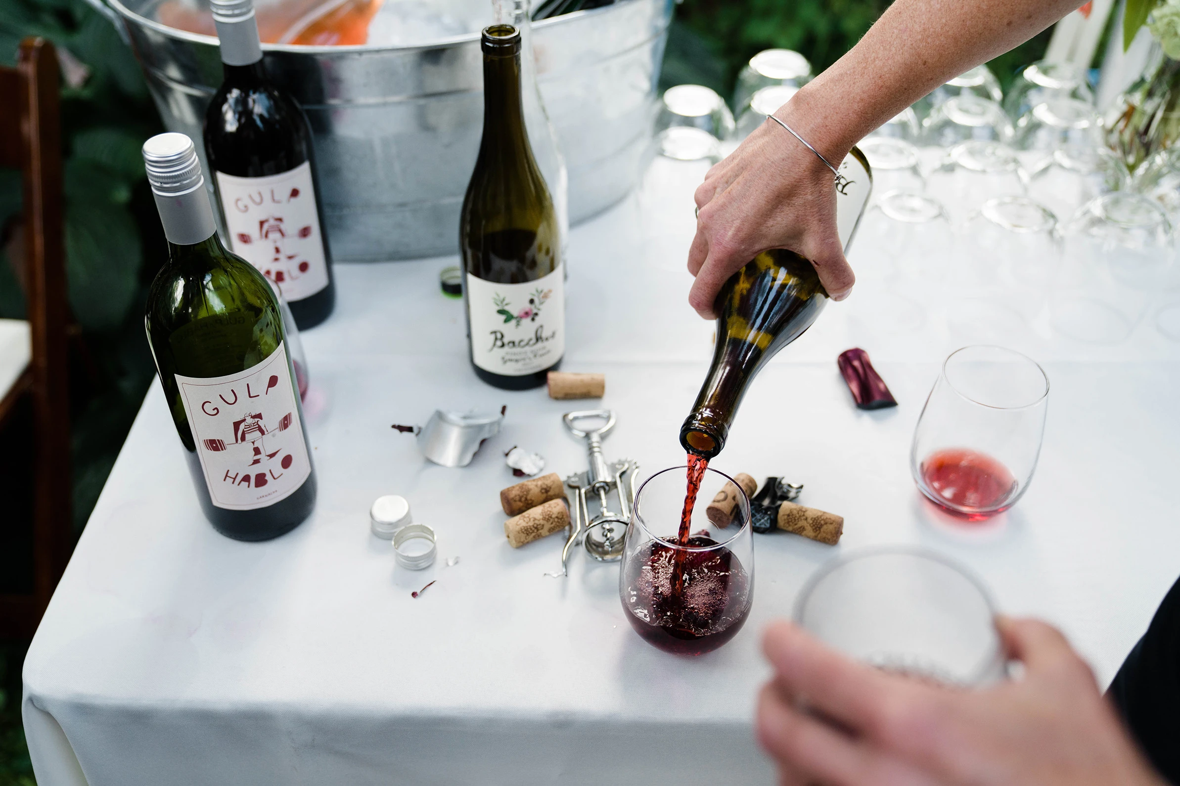 Red wine poured into glasses over a table of bottles