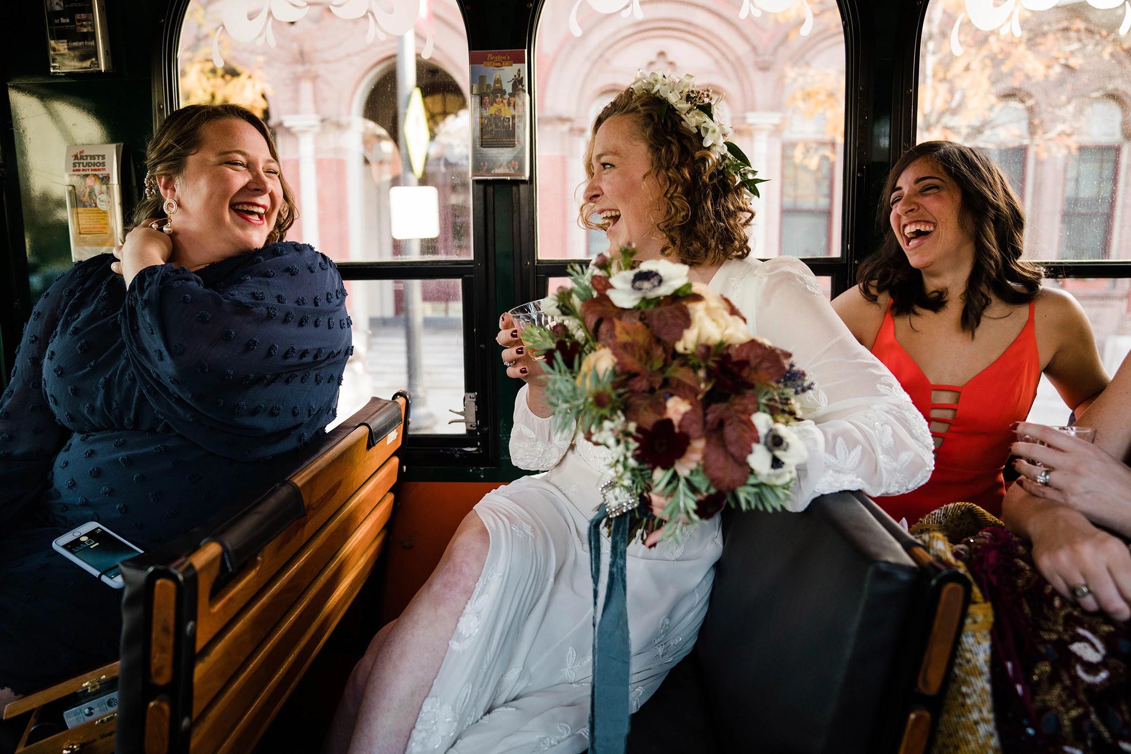 A bride with a bouquet laughing with two friends in a sunlit hall
