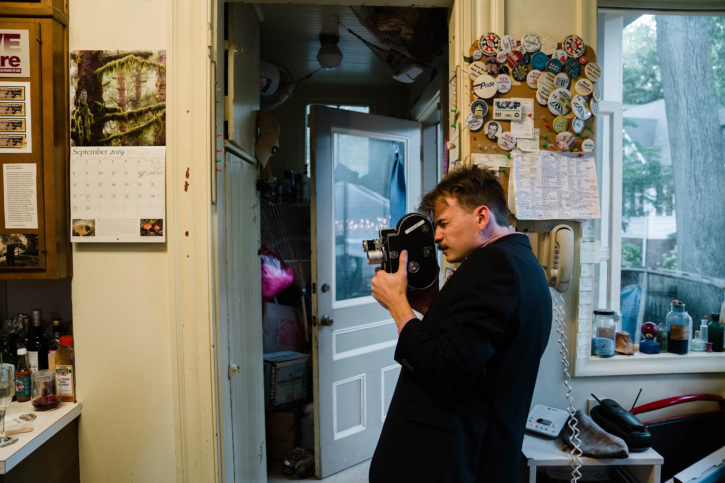 A videographer filming in a kitchen hung with notes and photos