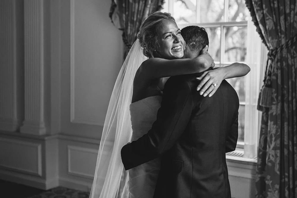 The bride hugging the groom by a tall window