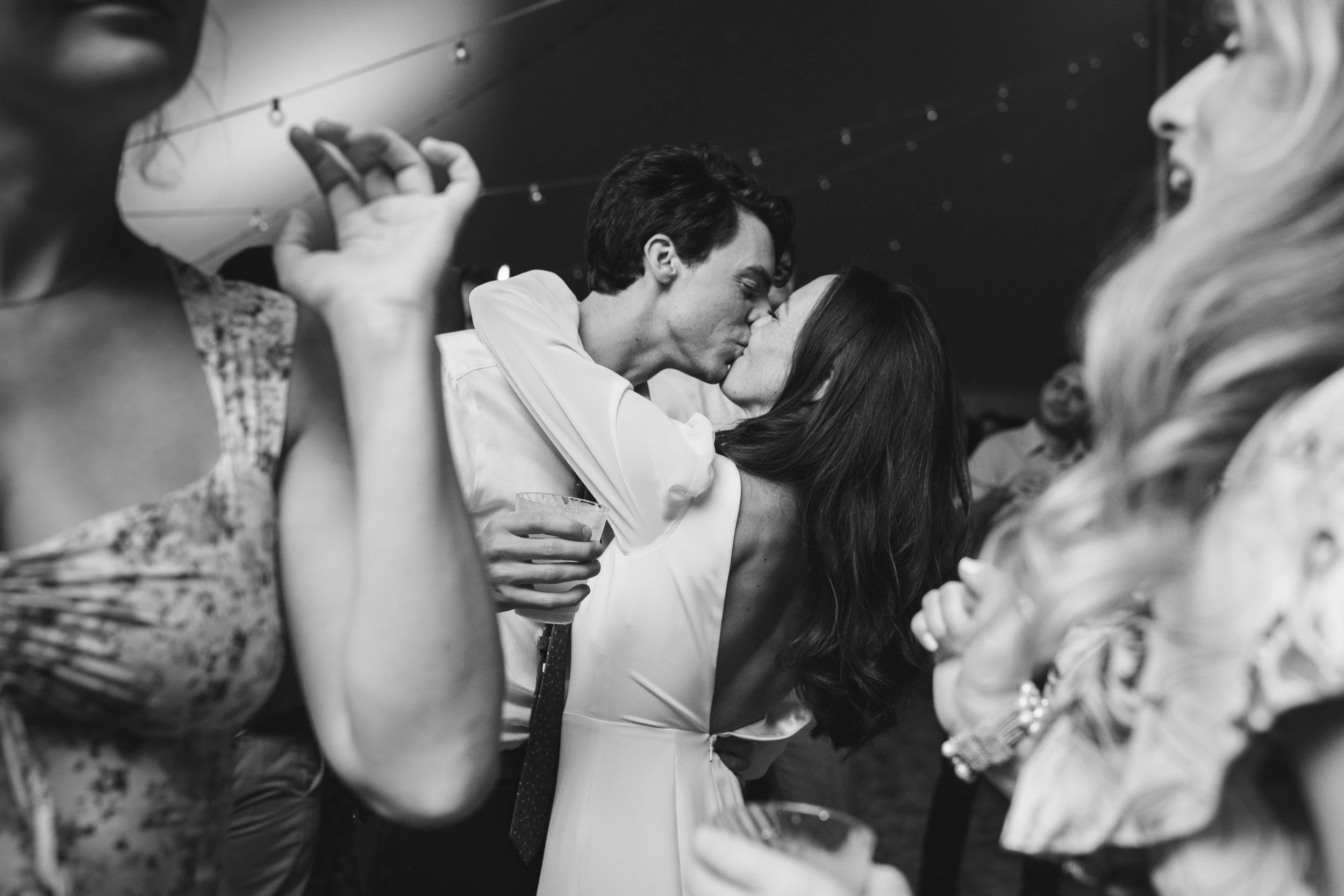 Couple kissing on a crowded dance floor, blurred guests in the foreground