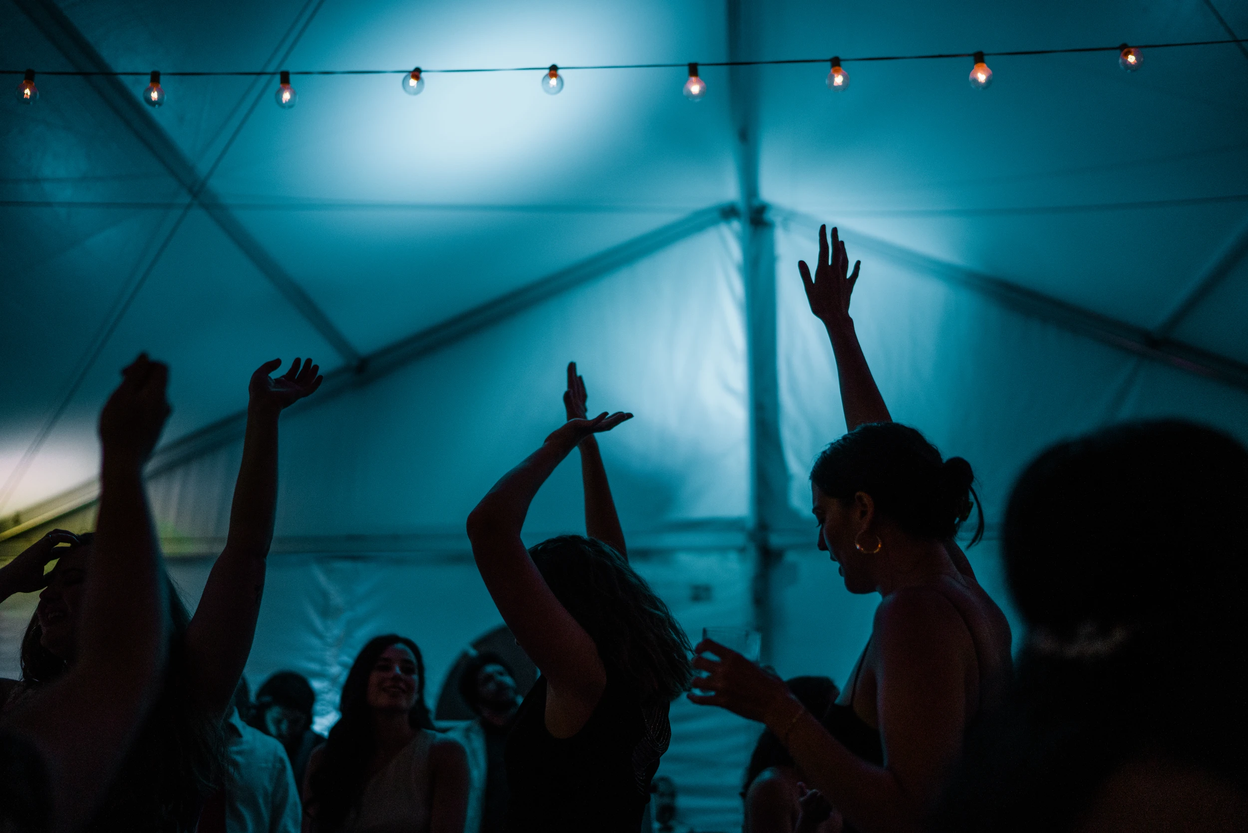 Guests dancing as silhouettes under a blue-lit tent
