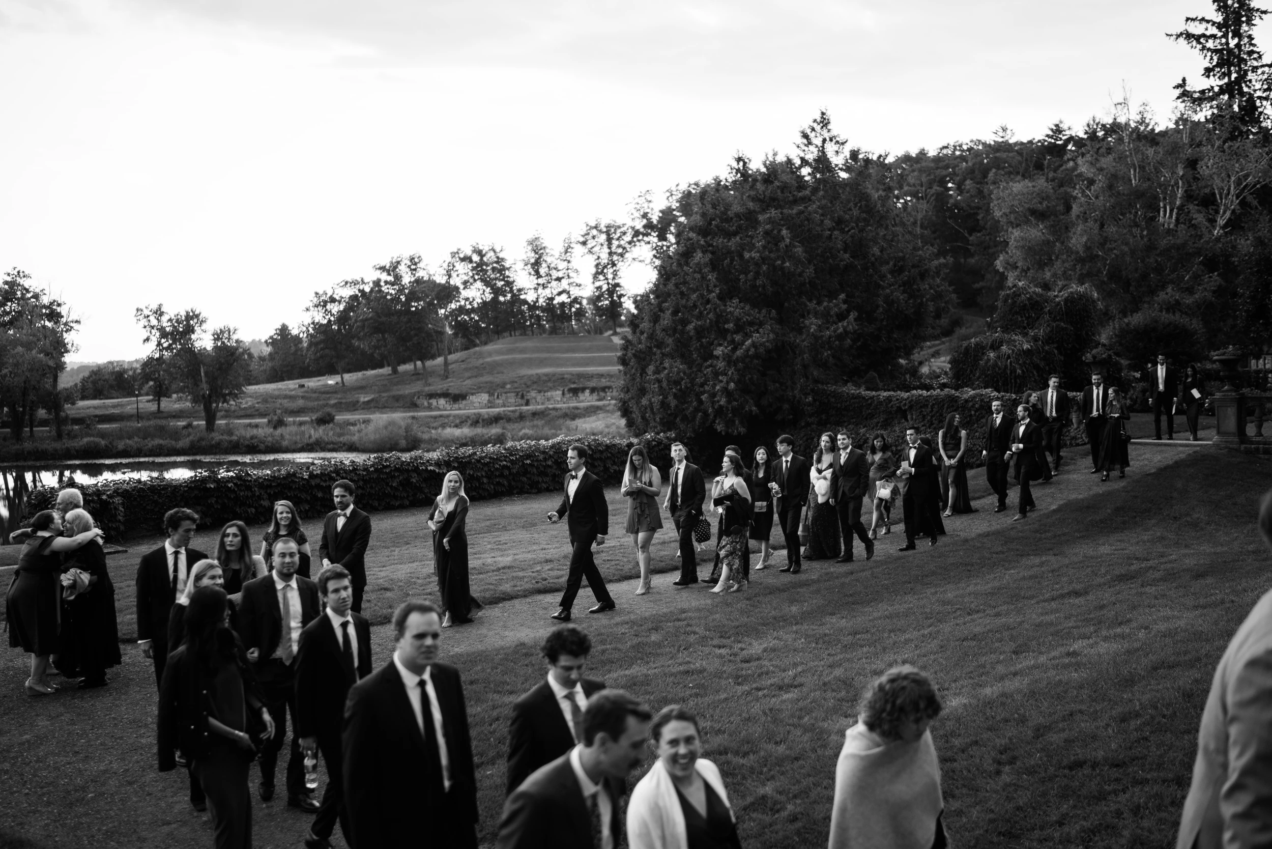 Guests walking across a wide lawn under a pale sky