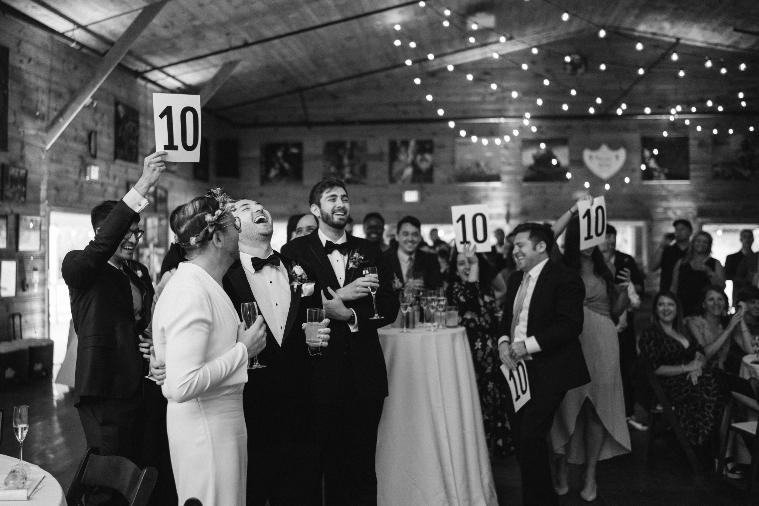 Guests packed around tables under string lights, table numbers raised