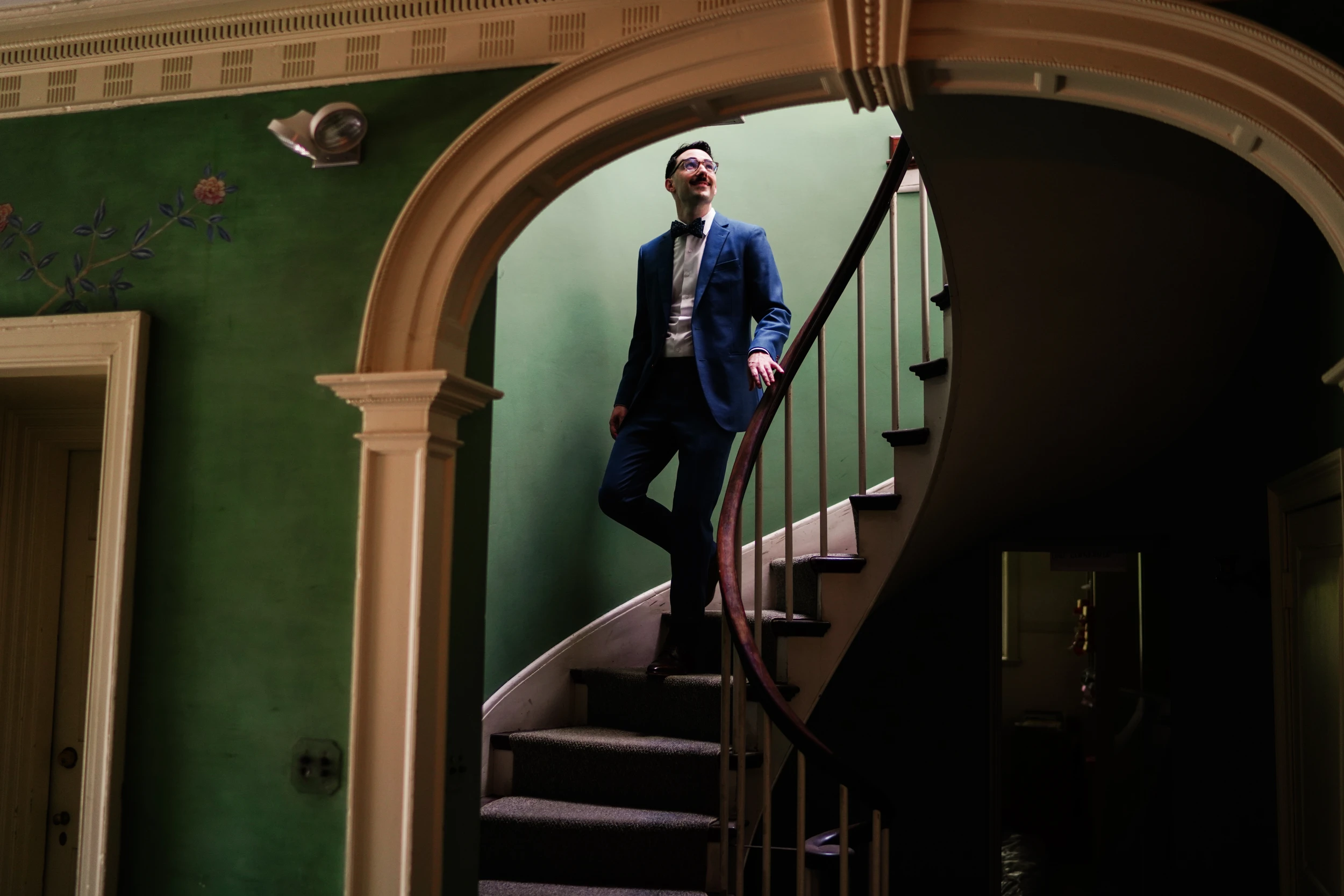 The groom climbing a spiral staircase in a green hallway