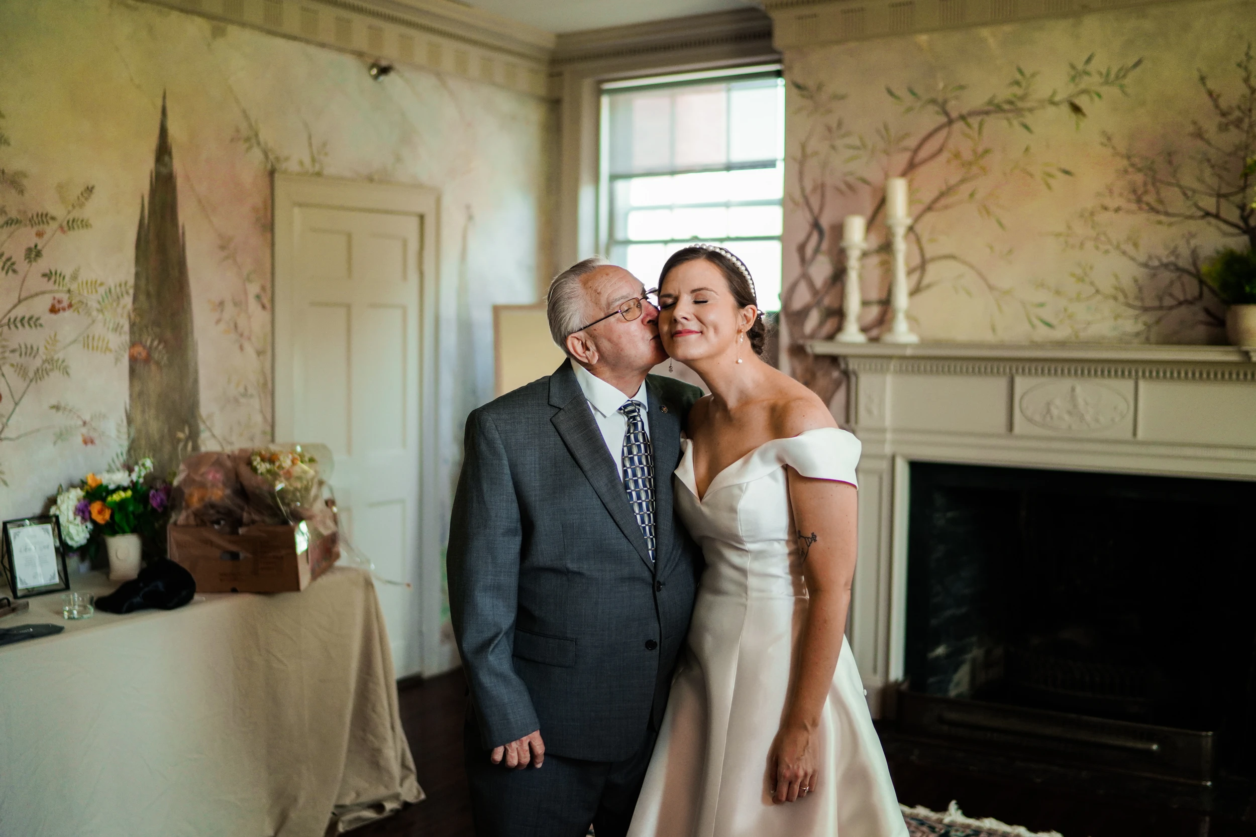 The bride and her father side by side by a fireplace
