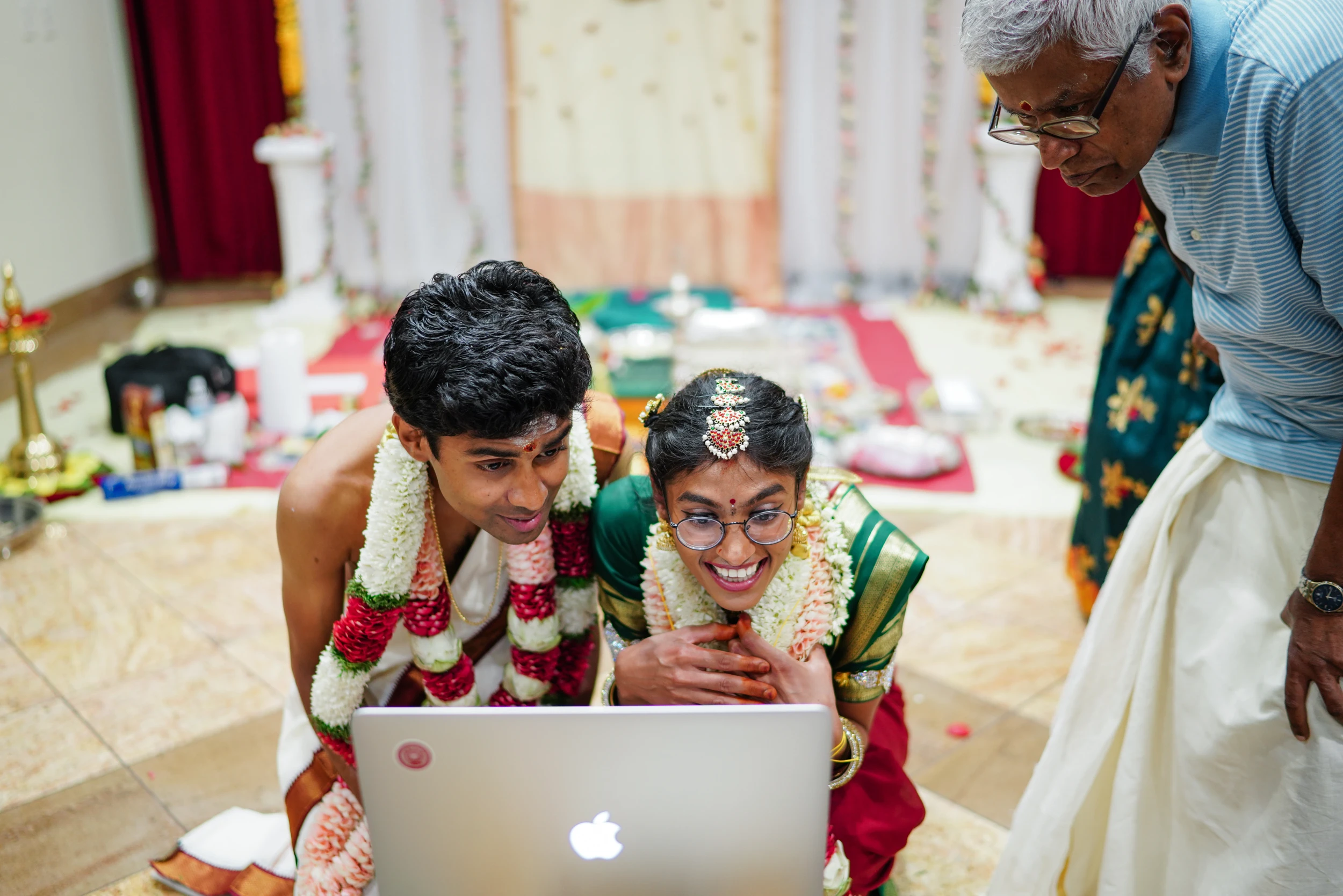 The couple in garlands smiling at a laptop during the ceremony