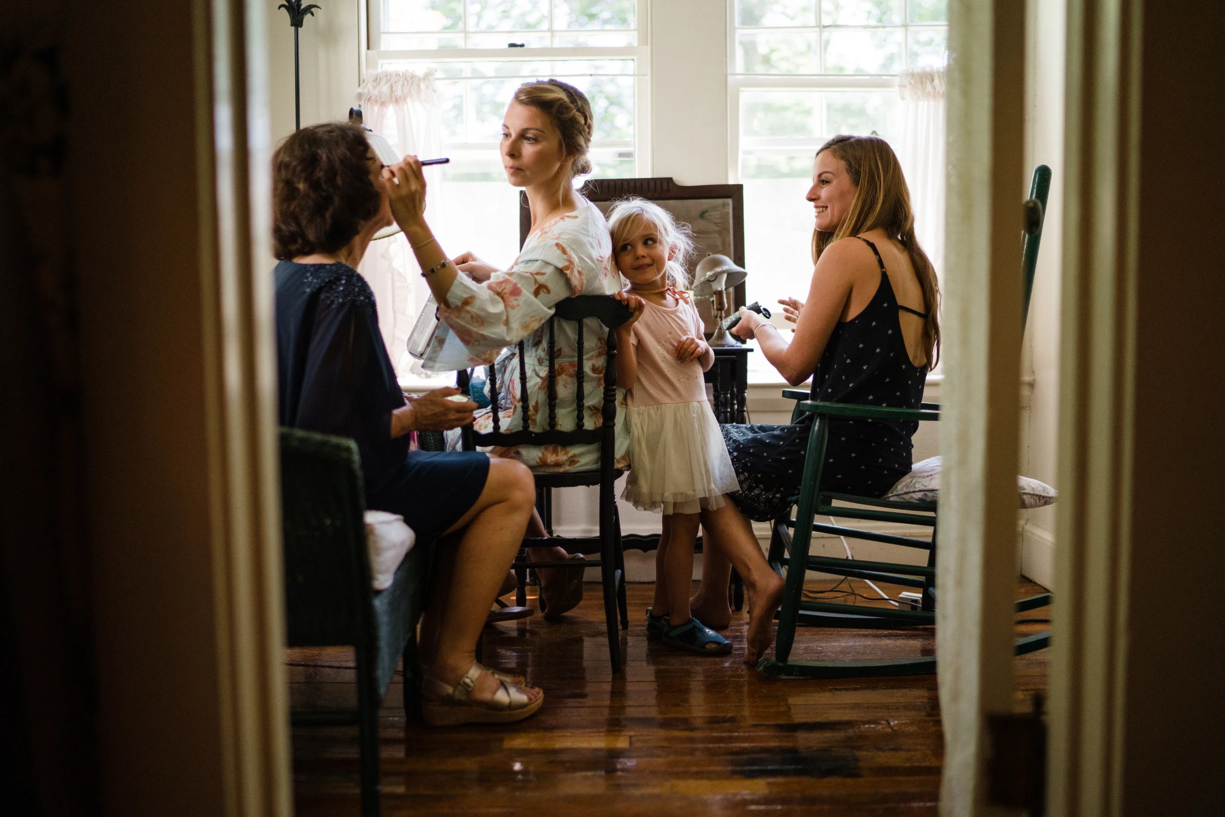 A mother doing makeup at a table, seen through a doorway, a small girl beside her